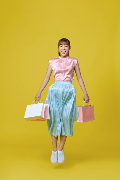 Full length profile of cute asian lady run with bags isolated on yellow background - Photo, Image