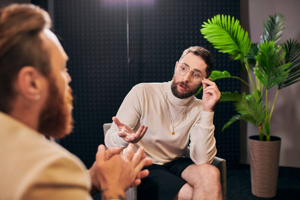 toegewijde elegante mannen in debonair kleding zitten en bespreken interview vragen in de studio - Foto, afbeelding
