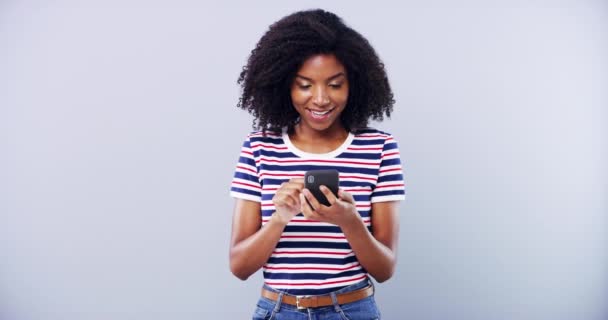 Чорна жінка, друкуючи по телефону і посміхаючись в студії, ізольована на білому фоні макет простору. Інтернет, смартфон і щаслива африканська людина прокручуються на мобільному додатку, електронній пошті або пошуку в Інтернеті в соціальних мережах. - Кадри, відео