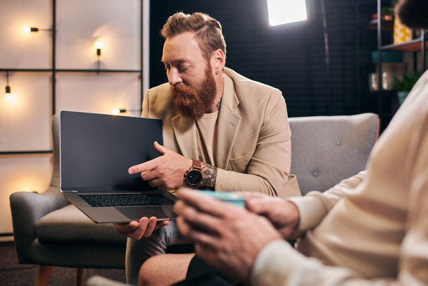 dobrze wyglądający modni mężczyźni w eleganckich strojach z kawą i laptopem omawiający pytania o wywiad - Zdjęcie, obraz