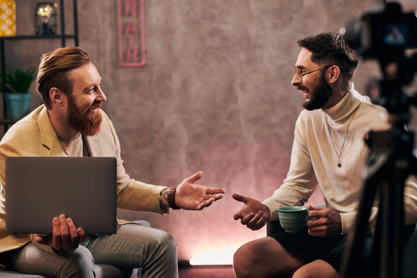 deux beaux hommes joyeux en tenues élégantes avec café et ordinateur portable discuter des questions d'entrevue - Photo, image