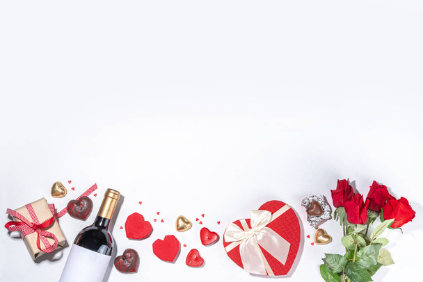 Ημέρα του Αγίου Βαλεντίνου ευχετήρια κάρτα επίπεδη θέσει. Ημέρα του Αγίου Βαλεντίνου απομονωμένο λευκό φόντο με μπουκάλι κρασί, σοκολάτες καρδιά γλυκά, μπουκέτο με κόκκινα τριαντάφυλλα, κουτί δώρου, καραμέλες σχήμα καρδιάς, κομφετί, χάντρες  - Φωτογραφία, εικόνα