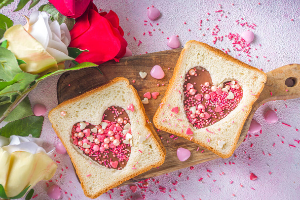 Aranyos édes reggeli szendvics. Kreatív ötlet Valentin napi nasira vagy ebédre. Pirítós szendvics mogyoróvajjal és csokis tésztával, Valentin-napi szívvel piros és rózsaszín cukorral. - Fotó, kép