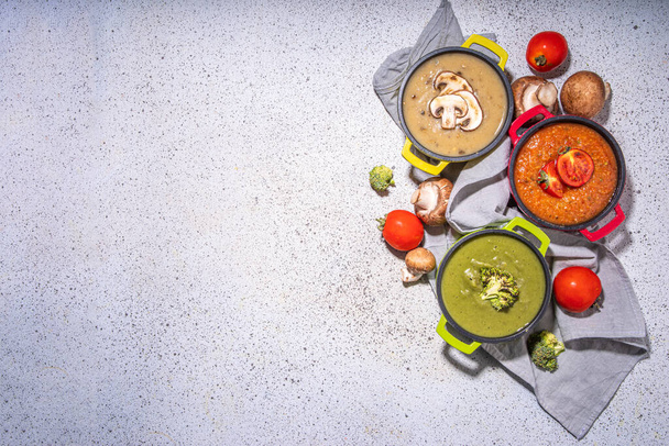 秋の野菜クリームスープセット. さまざまなビーガン熱い野菜クリームのスープのトマト,キノコ,白いテーブルのコピースペースのブロッコリーが付いている3つの部分の鍋 - 写真・画像