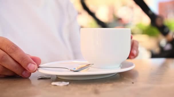 Kafe masasının üzerindeki beyaz seramik kahve bardağına seçici bir şekilde odaklan ve kadın elleri bardağı çıkarıp açık bir kafede sıcak kahve içmenin tadını çıkar. - Video, Çekim