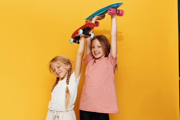 Διασκεδαστικές παιδικές αναμνήσεις: Αξιολάτρευτα κοριτσάκια αγκαλιάζουν το ένα το άλλο ενάντια σε ένα κομψό κίτρινο τοίχο - Φωτογραφία, εικόνα