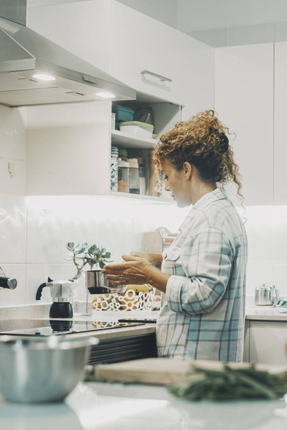 Μια γυναίκα που μαγειρεύει μόνη της στην κουζίνα. Πραγματικός ενιαίος τρόπος ζωής για ανεξάρτητες γυναίκες. Η νοικοκυρά ετοιμάζει γεύμα για την οικογένεια. Προβολή της κυρίας χρησιμοποιώντας κατσαρόλα και να προετοιμάσει τα τρόφιμα εσωτερική ζωή. - Φωτογραφία, εικόνα