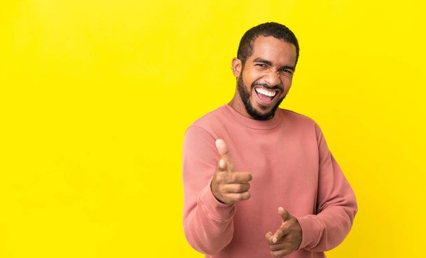Jonge Latijnse man geïsoleerd op gele achtergrond wijzend naar de voorkant en glimlachend - Foto, afbeelding