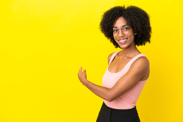 Jonge Afro-Amerikaanse vrouw geïsoleerd op gele achtergrond wijzend terug - Foto, afbeelding