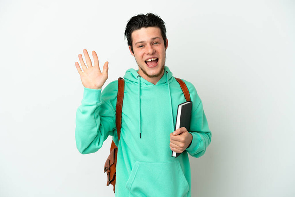 Joven estudiante aislado sobre fondo blanco saludando con la mano con expresión feliz - Foto, imagen