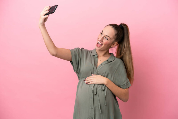 Young woman isolated on pink background pregnant and making a selfie - Photo, Image