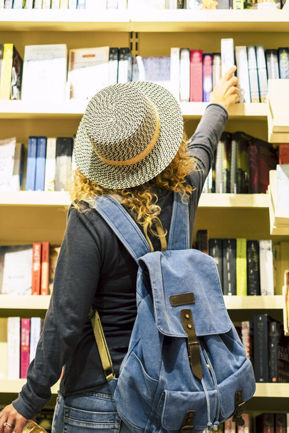 Sırt çantalı ve şapkalı bir kadının kütüphaneden ya da gazete dükkanından kitap seçmesi. İnsanlar seyahat etmeye hazırlanıyor. Boş zaman ve alışveriş, kadın aktiviteleri. Gezgin yaşam tarzı - Fotoğraf, Görsel