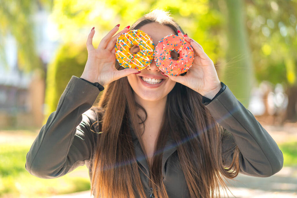 Açık havada genç bir kadın gözlerinde donut tutuyor. - Fotoğraf, Görsel