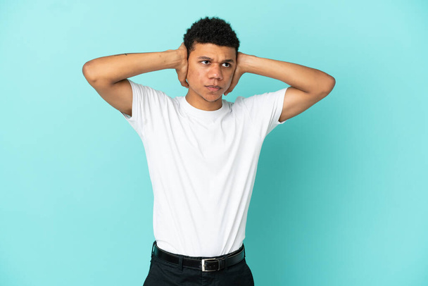 Young African American man isolated on blue background frustrated and covering ears - Фото, изображение