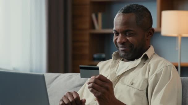 Χαμογελαστός αφρικανός αμερικανός άνδρας πελάτης πελάτης κάνει την πληρωμή της πιστωτικής κάρτας σε απευθείας σύνδεση χρήση lap-top απομακρυσμένη αγορά αμοιβής χρησιμοποιώντας την άμεση ασφαλή συναλλαγή από την τραπεζική εφαρμογή υπολογιστή που πληρώνει στο Διαδίκτυο - Πλάνα, βίντεο
