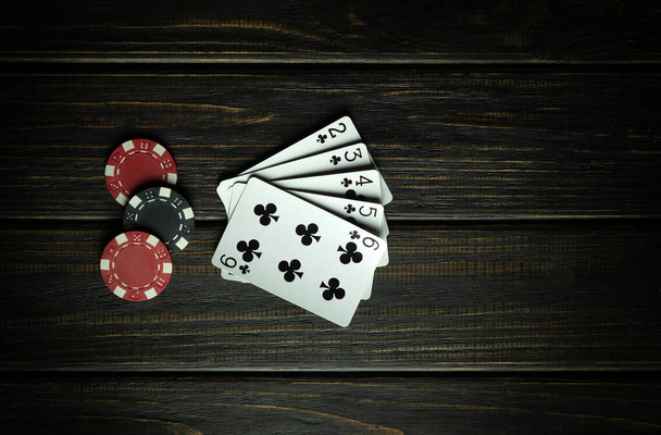 Gra w pokera z wygraną kombinacją strita-flush. Karty z żetonami na ciemnym stole vintage w klubie pokerowym. Wolne miejsce na reklamę - Zdjęcie, obraz