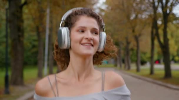 Sorridente donna spensierata ragazza positiva felice caucasico corridore femminile ascoltare la canzone in auricolari in esecuzione nel parco correre sorriso sport fitness attivo cardio formazione godere di musica audio moderno cuffie wireless - Filmati, video