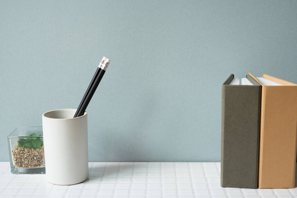 Werktafel met notitieblok, potloodhouder, potplant op wit tegelbureau. grijze muur achtergrond - Foto, afbeelding