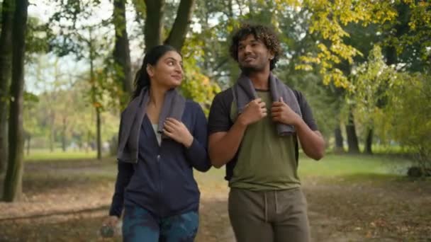 Indian man with Arabian woman friends wife husband girl guy guy girlfriend walking together after running workout sport training outdoors in forest park nature talking friendly communicating - Materiał filmowy, wideo