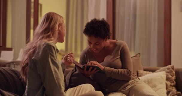 Valós idejű kézi lövés fiatal fekete nő olvasás könyv és csevegés barátnőjével, miközben jól érzik magukat együtt este otthon - Felvétel, videó