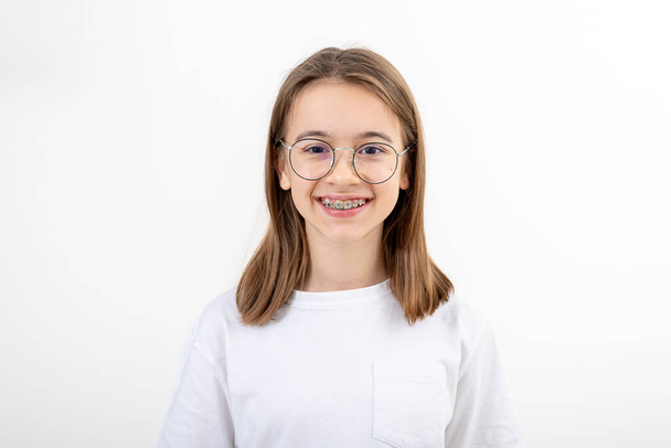 Tinédzser lány fehér pólóban, szemüveggel és fogszabályzóval a fogain, fehér alapon elszigetelve.. - Fotó, kép