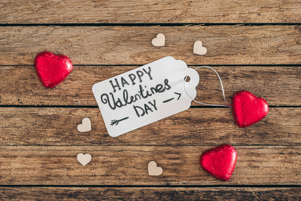 Üstünde "Sevgililer Günün kutlu olsun" yazan hediye etiketi ve tahta arka planda kalp şeklinde şekerler, üst manzara. Sevgililer Günü için yaratıcı arkaplan. - Fotoğraf, Görsel