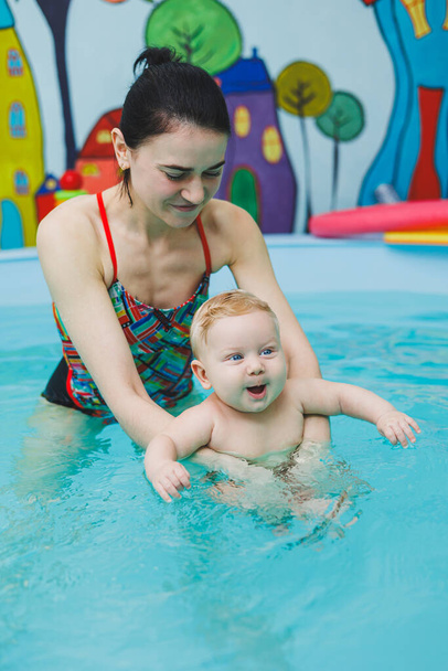 Vauva oppii uimaan altaassa valmentajan kanssa. Vauva opettelee uimaan. Lapsen kehitys. - Valokuva, kuva