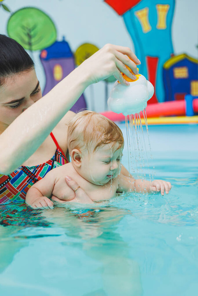 Vauva oppii uimaan altaassa valmentajan kanssa. Vauva opettelee uimaan. Lapsen kehitys. - Valokuva, kuva
