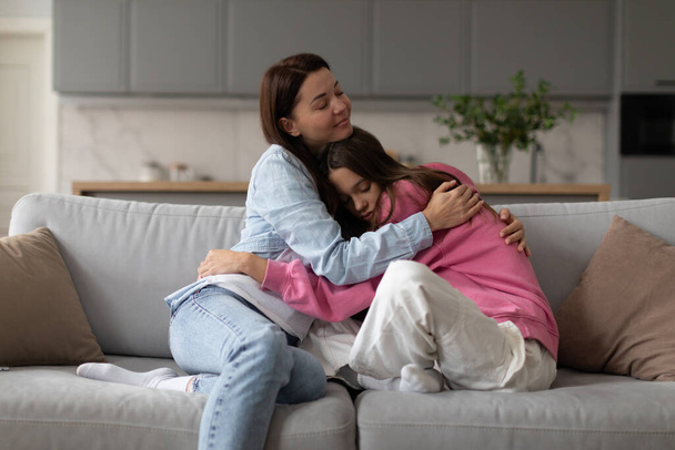 Szerető anya ölelés tini lánya, anya bemutató megértés és támogatás, hogy ideges szomorú tizenéves lány, ül együtt kanapén otthon - Fotó, kép