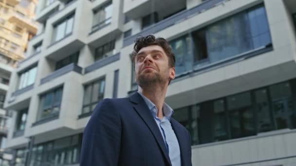 Businessman looking around urban district close up. Interested male customer contemplating modern residential area choosing place to live. Handsome elegant man standing street. Camera moving around. - Footage, Video