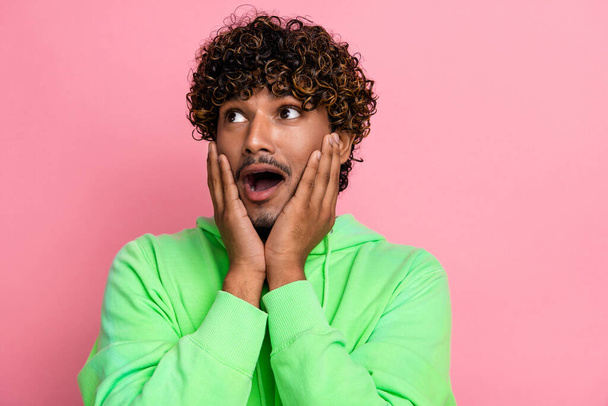 Photo of impressed speechless curly funny indian man in green sweatshirt touch cheeks look empty space isolated on pink color background. - Fotó, kép