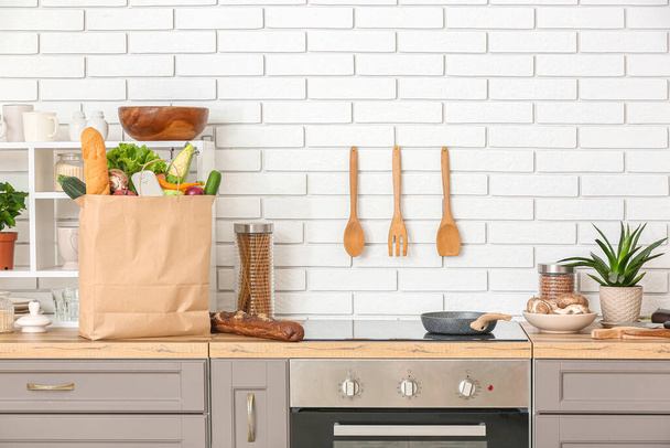 Bolsa de papel con diferentes productos y utensilios en el mostrador en la cocina - Foto, Imagen