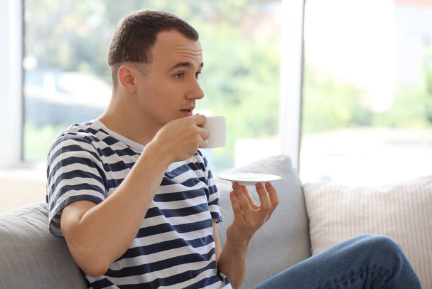 Νεαρός άνδρας πίνει καφέ στον καναπέ στο σπίτι - Φωτογραφία, εικόνα