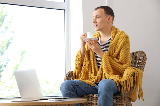 Junger Mann mit Karo und Tasse Kaffee sitzt zu Hause im Sessel - Foto, Bild