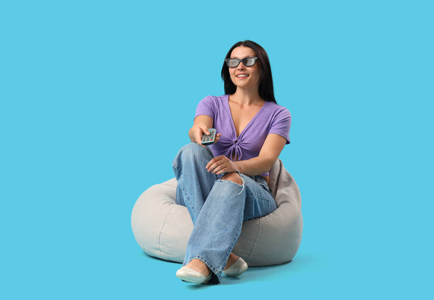 Pretty young woman in 3D glasses watching TV on blue background - Photo, Image