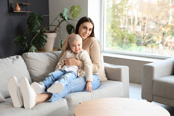 Маленька дівчинка після хіміотерапії зі своєю матір'ю сидить на дивані вдома - Фото, зображення