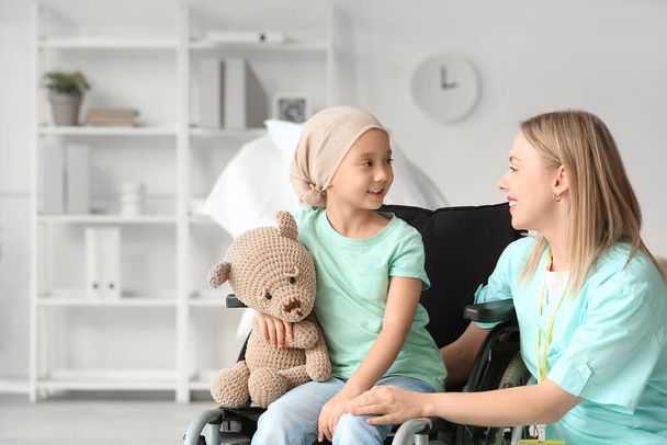 Μικρό ασιατικό κορίτσι μετά από χημειοθεραπεία σε αναπηρική καρέκλα με αρκουδάκι παιχνίδι και νοσοκόμα στο νοσοκομείο - Φωτογραφία, εικόνα