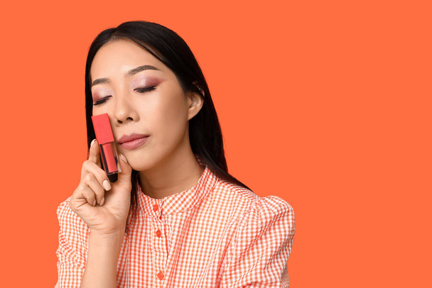 Gyönyörű ázsiai nő folyékony rúzs narancssárga háttér - Fotó, kép