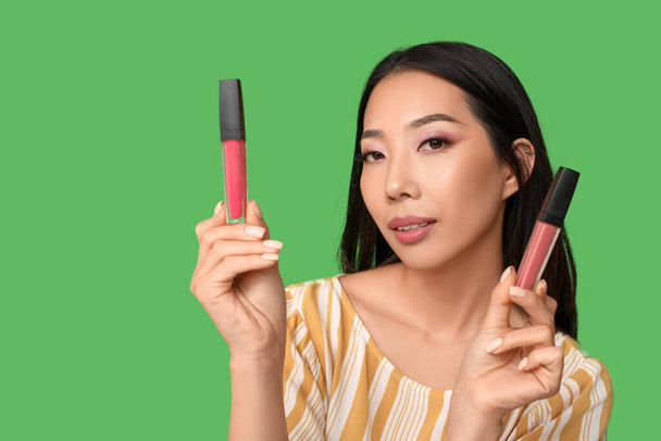 Beautiful Asian woman with different lipsticks on green background - Photo, Image