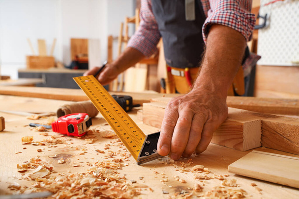 Ώριμος ξυλουργός μέτρησης ξύλινη σανίδα στο τραπέζι στο κατάστημα, closeup - Φωτογραφία, εικόνα