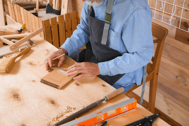 carpinteiro maduro desenho em caderno com régua à mesa na loja, close-up - Foto, Imagem
