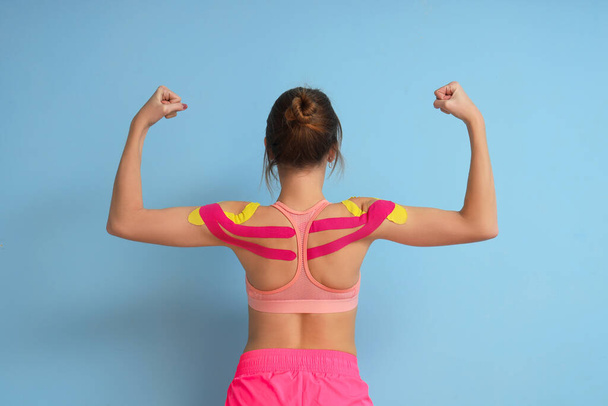 Mujer joven con cinta adhesiva que muestra los músculos sobre fondo azul, vista posterior - Foto, imagen