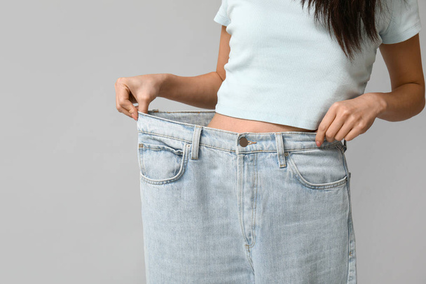Красива молода азіатка у вільних джинсах на сірому фоні, крупним планом - Фото, зображення
