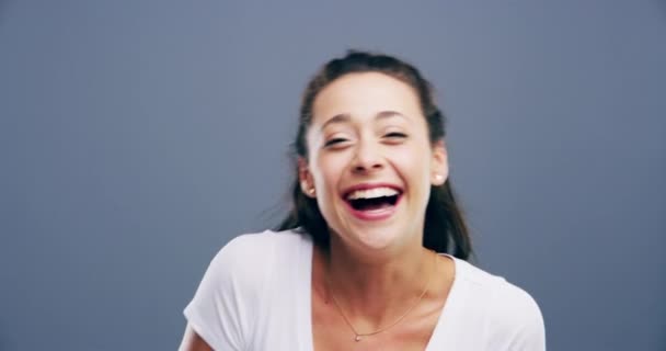 Face, funny and woman laughing in studio for humor, silly joke and good mood on grey background. Portrait, model and smile with cheerful personality for comedy, expression and reaction to crazy news. - Footage, Video