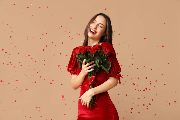 Mooie jonge vrouw met boeket van rode rozen en confetti op bruine achtergrond. Valentijnsdag - Foto, afbeelding
