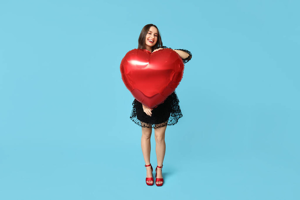 Beautiful young woman with heart shaped air balloon on blue background. Valentine's Day celebration - Fotografie, Obrázek