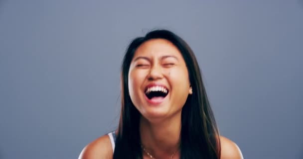 Arc, mosoly és ázsiai nő nevet a stúdióban humor, vicc és jókedv szürke háttér. Portré, boldog modell és vidám személyiség a komédiához, kifejezéshez és vicces reakcióhoz a buta hírekre. - Felvétel, videó
