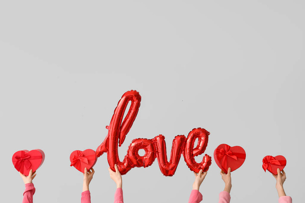 Manos femeninas con cajas de regalo y globos aéreos en forma de palabra AMOR sobre fondo gris. Celebración de San Valentín - Foto, imagen