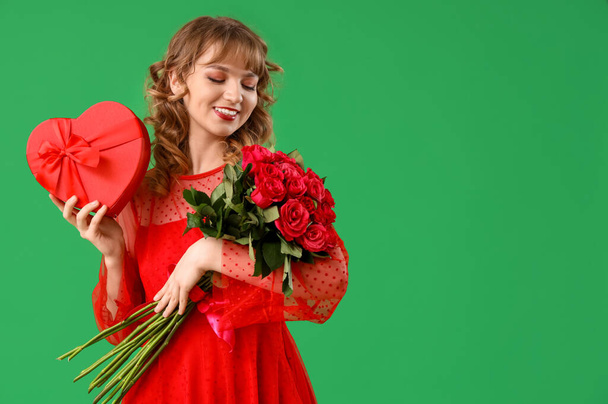 Schöne junge Frau mit Strauß roter Rosen und Geschenkbox auf grünem Hintergrund. Valentinstag-Feier - Foto, Bild