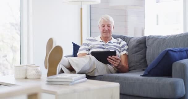 Relaks, tablet i starszy mężczyzna na kanapie z mediów społecznościowych, wyszukiwania lub ebook w swoim domu. Uśmiech, odpoczynek i stary mężczyzna z cyfrowym, aplikacja lub zakupy online, przewiń lub sprawdź usługę streaming. - Materiał filmowy, wideo